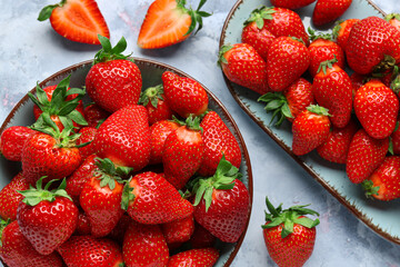 Bowl and plate with fresh strawberries on blue background