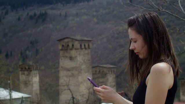 Young woman taking pictures of old stone towers in the mountains. View of traditional ancient Georgian architecture in Svaneti. Cultural heritage