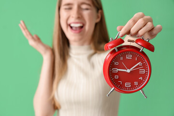 Stressed young woman with alarm clock on green background, closeup. Deadline concept