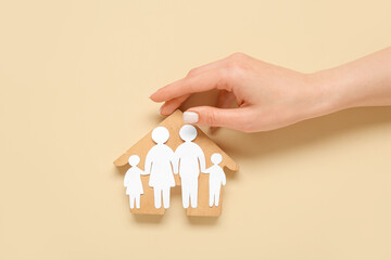 Female hand with figures of family and wooden house on beige background