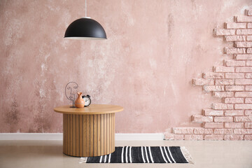 Wooden coffee table with alarm clock and home decor in room near grunge pink wall