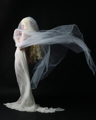 Full length portrait of beautiful blonde woman wearing white gown dress with flowing ghostly veiled...