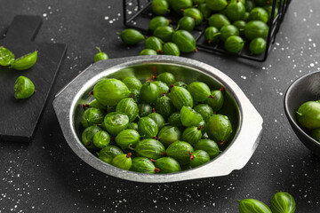 Metal plate with fresh gooseberries on black background