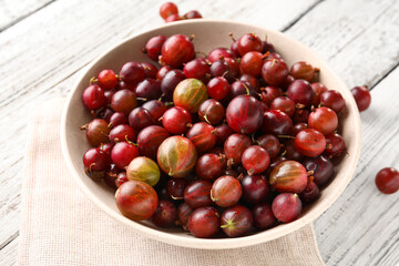 Bowl with fresh gooseberries on white wooden background