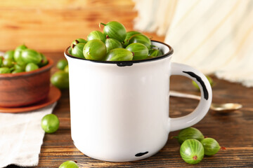Cup and bowl with fresh gooseberries on wooden background