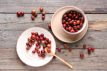 Bowl and plate with fresh gooseberries on grey wooden background