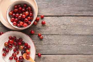 Bowl and plate with fresh gooseberries on grey wooden background