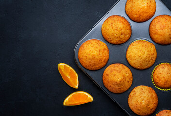 Sweet muffins with oranges and candied fruit in baking dish on black table background, homemade...
