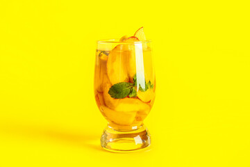 Glass of fresh peach lemonade with mint on yellow background
