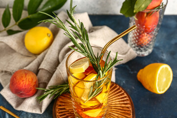 Wooden board with glass of fresh peach lemonade and rosemary on blue table