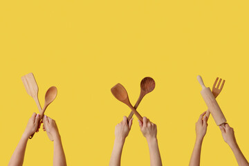Female hands with wooden baking utensils on yellow background