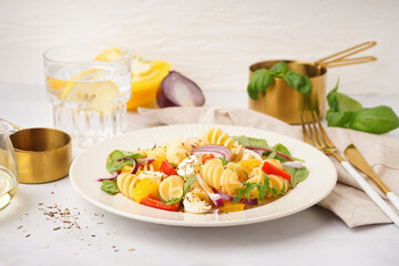Plate of tasty pasta salad with pepper and red onion on white background