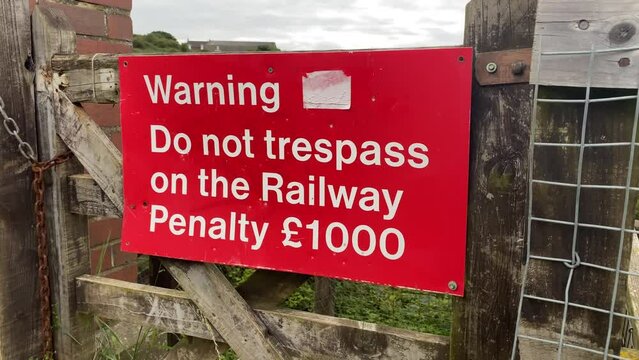 A red sign next to a railway line warning people not to trespass on the railway. Penalty of £1000.