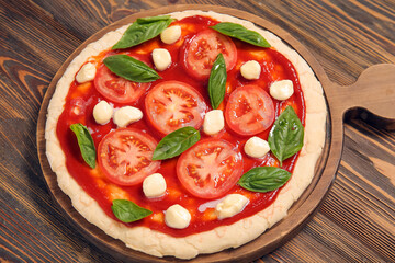 Board of pizza dough with tomato sauce and ingredients on wooden background