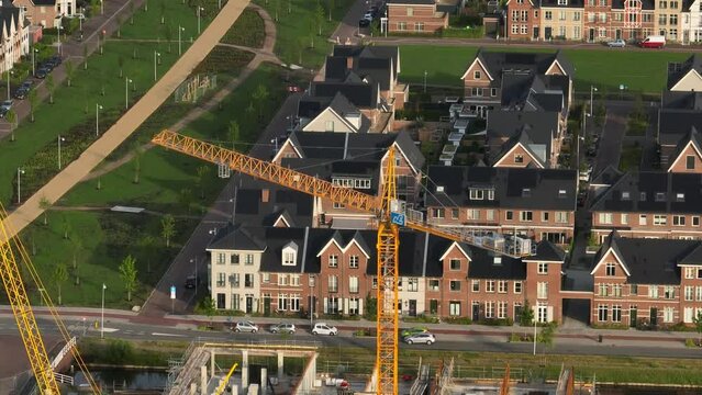 Medium aerial orbiting view of a yellow tower crane building a new housing development in teh town of Weesp near Amsterdam, Netherlands