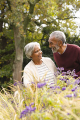 Happy senior biracial couple holding hands and smiling at each other in garden at home