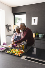 Happy senior biracial couple embracing and preparing vegetables in kitchen at home, copy space