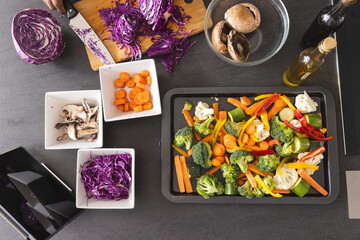 Overhead of senior biracial woman cutting cabbage on table with vegetables in kitchen at home