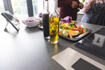 Midsection of senior biracial couple using tablet preparing vegetables in kitchen at home