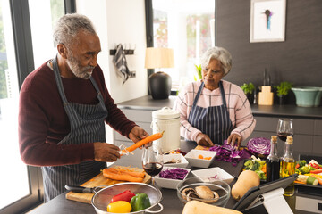 Senior biracial couple wearing aprons preparing vegetables and using tablet in kitchen at home © wavebreak3
