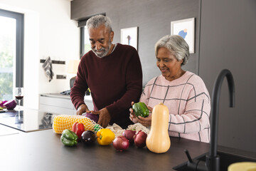 Happy senior biracial couple unpacking bags of vegetables in kitchen at home - Powered by Adobe