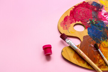 Brushes and palette with paints on pink background, closeup
