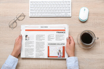 Woman reading newspaper at workplace with cup of coffee on wooden background