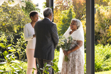 Happy biracial female marriage officiant and senior couple during wedding in sunny garden