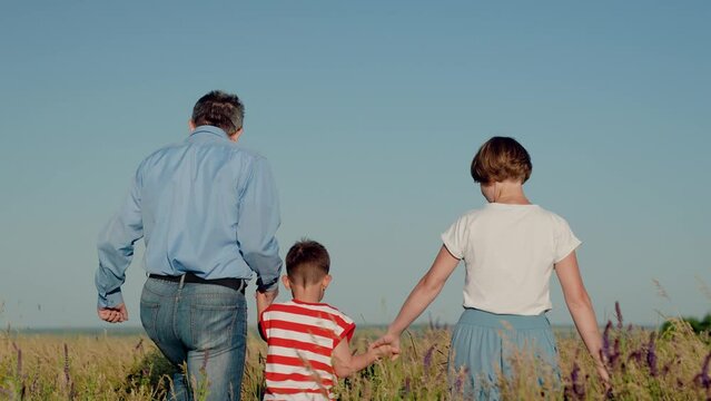 father mother child friendly family, holding hands child parents walk through flowering green grass park, family teamwork nature, family path success, mother father holding little son by hand, walking