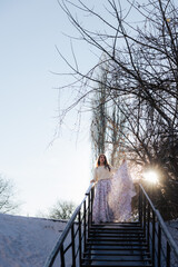 The girl goes down the stairs in a long dress at sunset