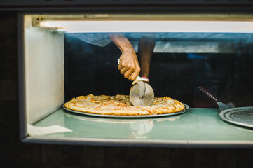 Multicultural hand slices pizza in a NYC 99 cent pizza shop