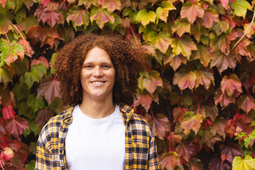 Portrait of happy biracial man with red curly hair standing in autumn garden smiling, copy space