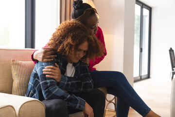 Sad diverse couple sitting in living room at home, embracing and comforting