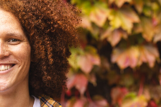 Half portrait of happy biracial man with red curly hair smiling in autumn garden, copy space - Powered by Adobe