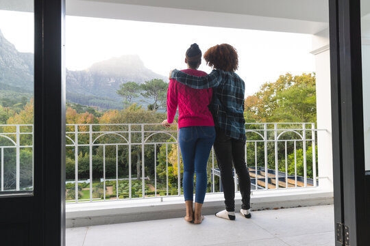 Rear view of happy diverse couple on balcony embracing and admiring view at home, copy space