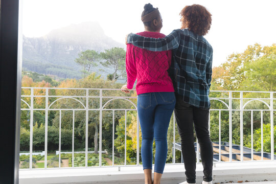Rear view of happy diverse couple on balcony embracing and admiring view at home, copy space - Powered by Adobe