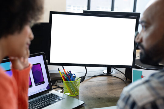 Rear view of diverse male and female designers discussing at computer with copy space in office