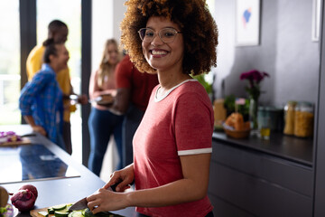 Portrait of happy biracial woman cutting vegetables with diverse friends in kitchen - Powered by Adobe