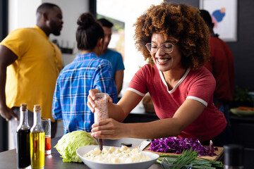 Happy diverse group of friends seasoning and cooking in kitchen
