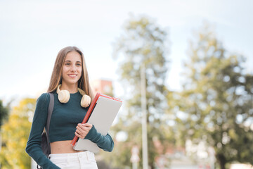 Teenage student holding laptop and notebooks, poses looking at camera on street. Smart girl with backpack smiling. Proud and satisfied teenager on her way to high school.