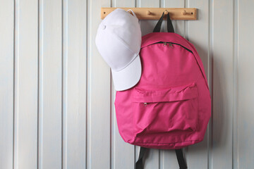 pink school backpack and a white baseball cap are hanging on a hanger .