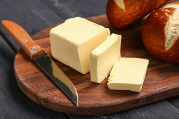 Board with fresh butter and bread on black wooden background