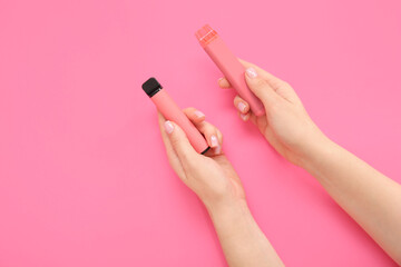 Woman holding electronic cigarettes on pink background