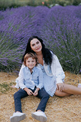 Naklejka na ściany i meble Smiling mother and son sitting on hay near blooming lavender.