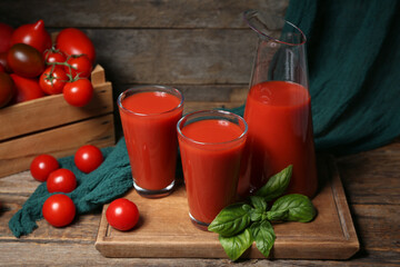 Glasses and jug of tomato juice on wooden background