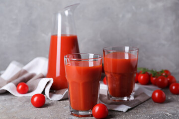 Glasses of tasty tomato juice on grey background