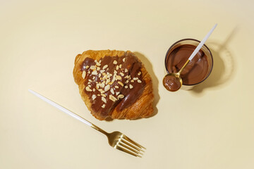 Sweet croissant and glass of chocolate on beige background