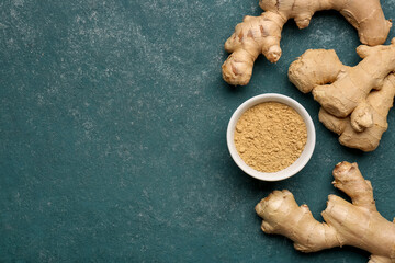 Fresh ginger roots and bowl with dried powder on blue background
