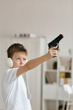 Picture of boy wearing white T-shirt and headphones shooting toy gun with serious face expression