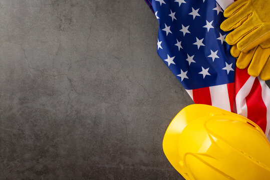 Commemorating the significant contributions of construction workers on American Labor Day. Above shot of flag, helmet and gloves on grunge textured grey concrete. Suitable for ads or text - Powered by Adobe
